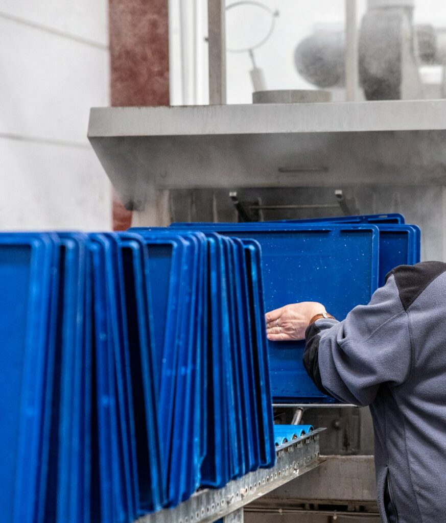 Professionnels en action lors du nettoyage et de la désinfection des bacs EURO dans un tunnel de lavage respectant les normes d'hygiène et de sécurité alimentaire