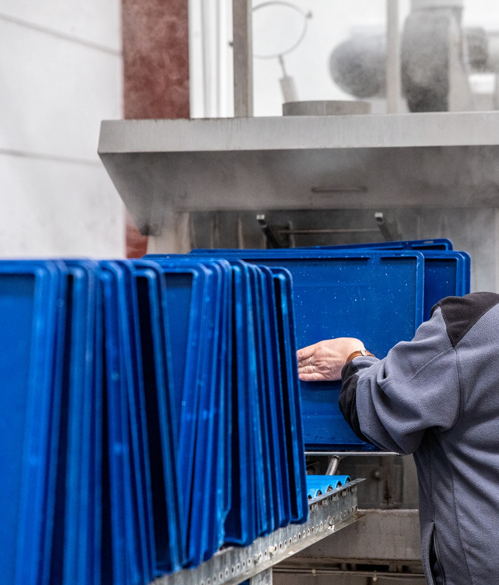 Professionnels en action lors du nettoyage et de la désinfection des bacs EURO dans un tunnel de lavage respectant les normes d'hygiène et de sécurité alimentaire